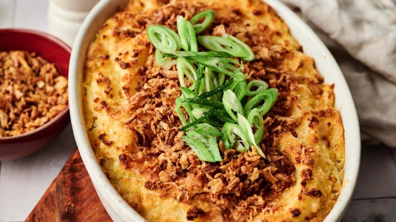 Golden baked mashed potato casserole topped with crispy fried onions and sliced green onions, in a white baking dish